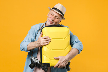 Happy traveler tourist elderly gray-haired man in hat photo camera isolated on yellow background. Passenger traveling to travel abroad on weekends getaway. Air flight journey concept. Hold suitcase.