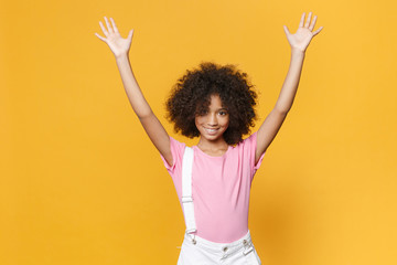 Smiling little african american kid girl 12-13 years old in pink t-shirt isolated on yellow background children studio portrait. Childhood lifestyle concept. Mock up copy space Rising spreading hands.