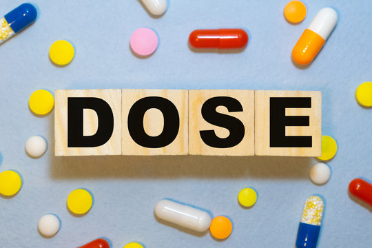 Wooden Cubes With Word Dose Color Pills And Syringe With Red Medicine On Light Green Table Closeup