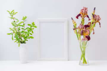 Home interior with decor elements. Mockup with a white frame and bouquet of irises flowers in a glass vase on a light background