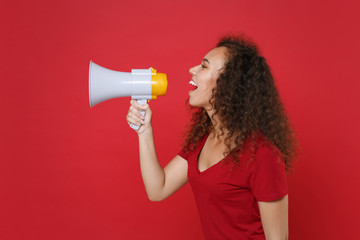 Side view of funny young african american woman girl in casual t-shirt posing isolated on red background studio portrait. People emotions lifestyle concept. Mock up copy space. Screaming in megaphone.