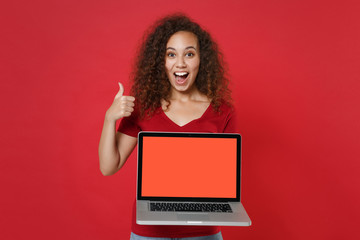 Naklejka premium Excited young african american woman girl in casual t-shirt isolated on red background. People lifestyle concept. Mock up copy space. Hold laptop pc computer with blank empty screen, showing thumb up.