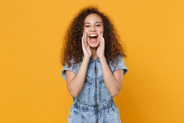 Cheerful young african american woman girl in casual denim clothes isolated on yellow wall background studio. People lifestyle concept. Mock up copy space. Screaming with hands gesture near mouth.