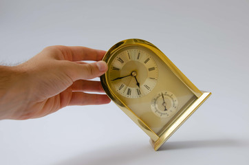 Golden alarm clock hand. A man holds a gilded home watch. Golden clock white background.