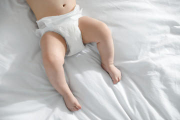 Little baby in diaper lying on bed at home, closeup view