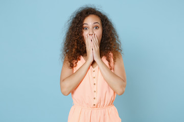 Shocked young african american woman girl in pastel summer clothes posing isolated on blue background studio portrait. People emotions lifestyle concept. Mock up copy space. Covering mouth with hands.
