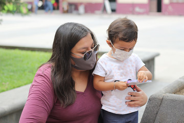 mom and 2-year-old latin girl with protective masks walking in the plaza, new normal covid-19