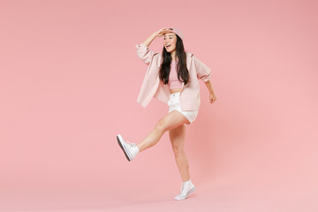 Full length portrait of funny young asian girl in casual clothes, cap isolated on pink background. People lifestyle concept. Mock up copy space. Holding hand at forehead looking far away distance.