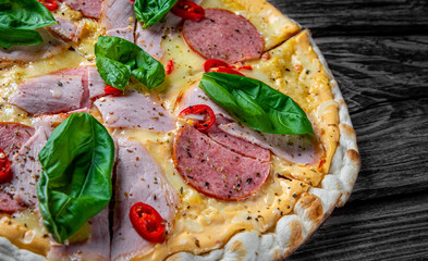 Pizza with Mozzarella cheese, ham, tomato sauce, salami, pepper, Spices and Fresh basil. Italian pizza on wooden table background