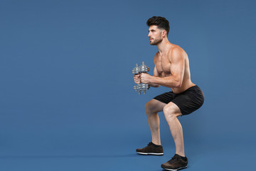 Full length portrait young fitness sporty strong guy bare-chested muscular sportsman isolated on blue background. Workout sport motivation lifestyle concept. Doing exercise squatting with dumbbells.
