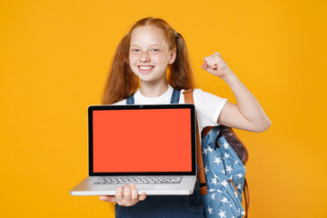 Naklejka premium Young redhead school girl 12-13 years old in white t-shirt blue denim uniform backpack hold laptop pc computer isolated on yellow background children studio portrait Kids education lifestyle concept