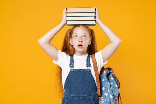 Young fun redhead girl 12-13 years old in white t-shirt backpack hold on head big stack school textbook notebook books isolated on yellow background children studio portrait Kids education concept