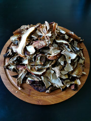 Chopped dried porcini mushrooms and boletus lie on a round wooden board on a black background.