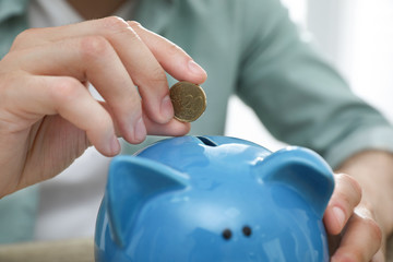 Man putting coin into piggy bank, closeup