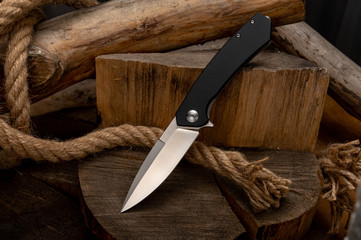 A sharp knife with a black handle on a stump with a rope.