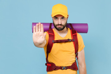 Serious traveler young man in yellow t-shirt cap with backpack isolated on blue background. Tourist traveling on weekend getaway. Tourism discovering hiking concept. Showing stop gesture with palm.
