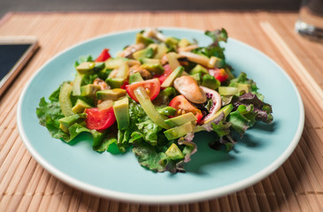 Salad with seafood with avocado, tomatoes, octopus and mussels in blue plate on wooden table. Concept of healthy diet food. Lunch or dinner after work.
