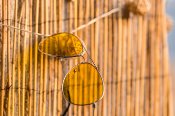 Retro aviator sunglasses model with big yellow lenses recommended for driving hanging on a bamboo fence closeup . Selective focus