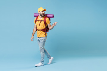 Full length portrait excited young traveler man in yellow t-shirt cap backpack isolated on blue background. Tourist traveling on weekend. Tourism discovering hiking concept. Point index finger aside.