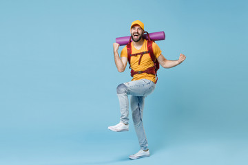 Full length portrait happy young traveler man in yellow casual t-shirt cap backpack isolated on blue background. Tourist traveling on weekend. Tourism discovering hiking concept. Doing winner gesture.