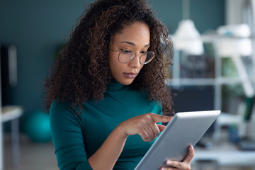 Concentrated young entrepreneur woman using her digital tablet while standing in the office.