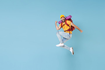 Fototapeta na wymiar Full length portrait Joyful young traveler man in cap with backpack isolated on blue background. Tourist traveling on weekend getaway. Tourism discovering hiking concept. Jump doing winner gesture.