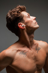 Naklejka premium Cool young guy in wireless earphone listen to song with naked torso. Music poster. Body with tattoo