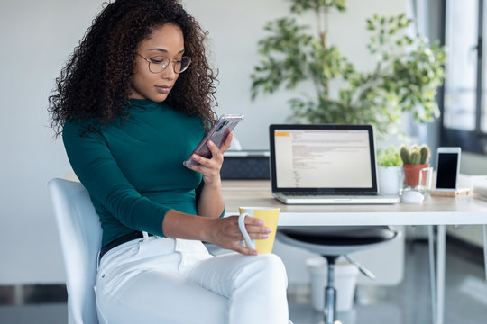 Confident young business woman sending messages with mobile phone sitting in the office.
