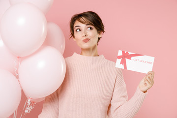 Pensive young brunette woman girl in knitted casual sweater posing isolated on pastel pink...