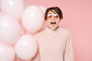Excited young brunette woman girl in knitted casual sweater glasses isolated on pastel pink background studio portrait. Birthday holiday party people emotions concept. Celebrating hold air balloons.