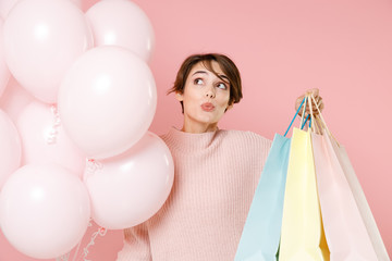 Pensive young woman girl in casual sweater isolated on pastel pink background. Birthday holiday party people emotions concept. Celebrating hold air balloons package bag with purchases after shopping.