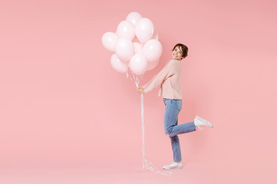 Full length portrait side view of smiling young woman in casual sweater isolated on pastel pink background. Birthday holiday party people emotions concept. Celebrating hold air balloons rising leg.