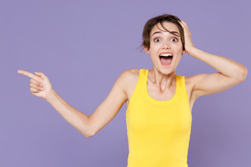 Surprised young brunette woman girl in yellow casual tank top posing isolated on pastel violet background. People lifestyle concept. Mock up copy space. Pointing index finger aside, put hand on head.