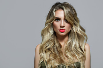 Blonde with curls on a gray background. Long hair. Red lipstick. Beautiful lips and big eyes....