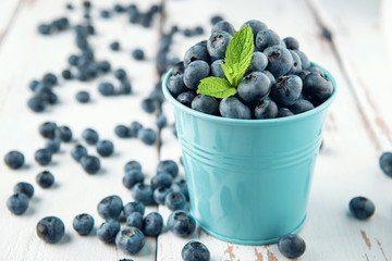 Small bucket with blueberry and mint leaves on white Provence style wooden table. Copy space.