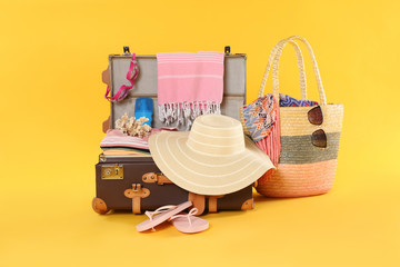 Bag and open vintage suitcase with different beach objects packed for summer vacation on orange...