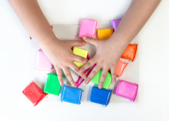 Greedy child covers with hands multi-colored plasticine. Multi-colored airy clay mass for modeling on a white background.