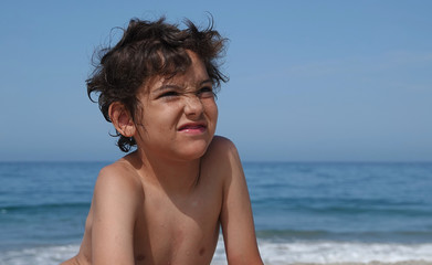 A young boy looks very unhappy at the idea of leaving the beach to go home - obrazy, fototapety, plakaty