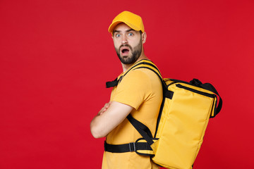 Side view delivery man 20s in yellow cap t-shirt thermal bag backpack with food isolated on red background studio Guy male employee work courier Service quarantine coronavirus covid-19 virus concept