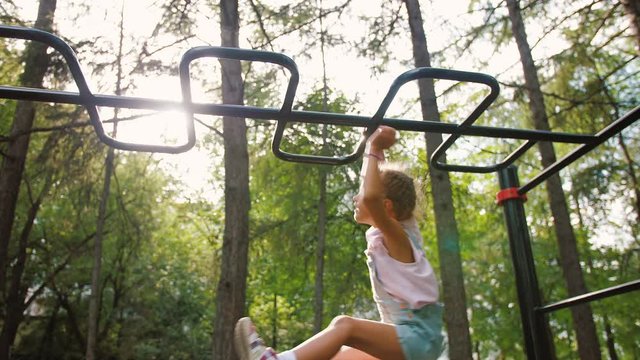 Little girl hanging and climbing on monkey bars in park on workout playground