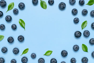 Fresh juicy blueberries with green leaves on blue background. Blueberries background. Flat lay top view copy space. Healthy berry, organic food, antioxidant, vitamin, blue food. Blueberry frame