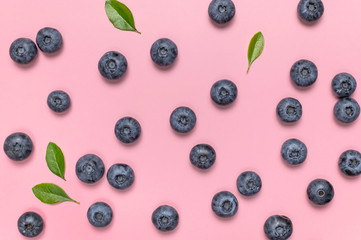 Fresh juicy blueberries with green leaves on pink background. Blueberries background. Flat lay top view copy space. Healthy berry, organic food, antioxidant, vitamin, blue food. Blueberry pattern