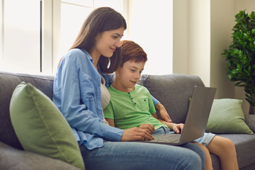 Young mother and her son talking to teacher from home. Parent and child watching online lesson on laptop computer