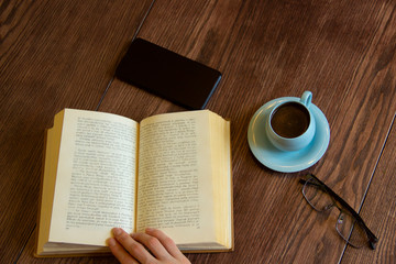 blue coffee cup, book, telephone, glasses on a brown wooden table