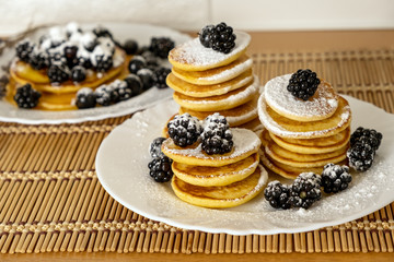 Dessert and breakfast concept. Sugar powder being poured over pancakes.Tasty breakfast food. Stack of american pancakes served with black currant and blackberry