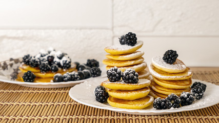 Dessert and breakfast concept. Sugar powder being poured over pancakes.Tasty breakfast food. Stack of american pancakes served with black currant and blackberry