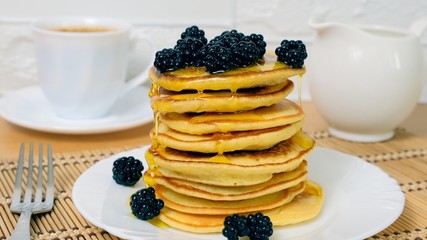 Pancakes. Sweet honey pouring over dessert with berry fruit. Tasty breakfast food. Stack of american pancakes served with black currant and blackberry