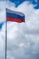 Russian tricolor flag waving in the wind against a cloudy sky.