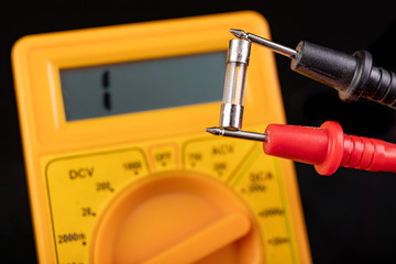 Voltmeter and glass fuse. Measurements and repairs in an electronics workshop.