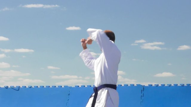 In karategi, an athlete performs formal karate exercises on a background of blue sky with clouds